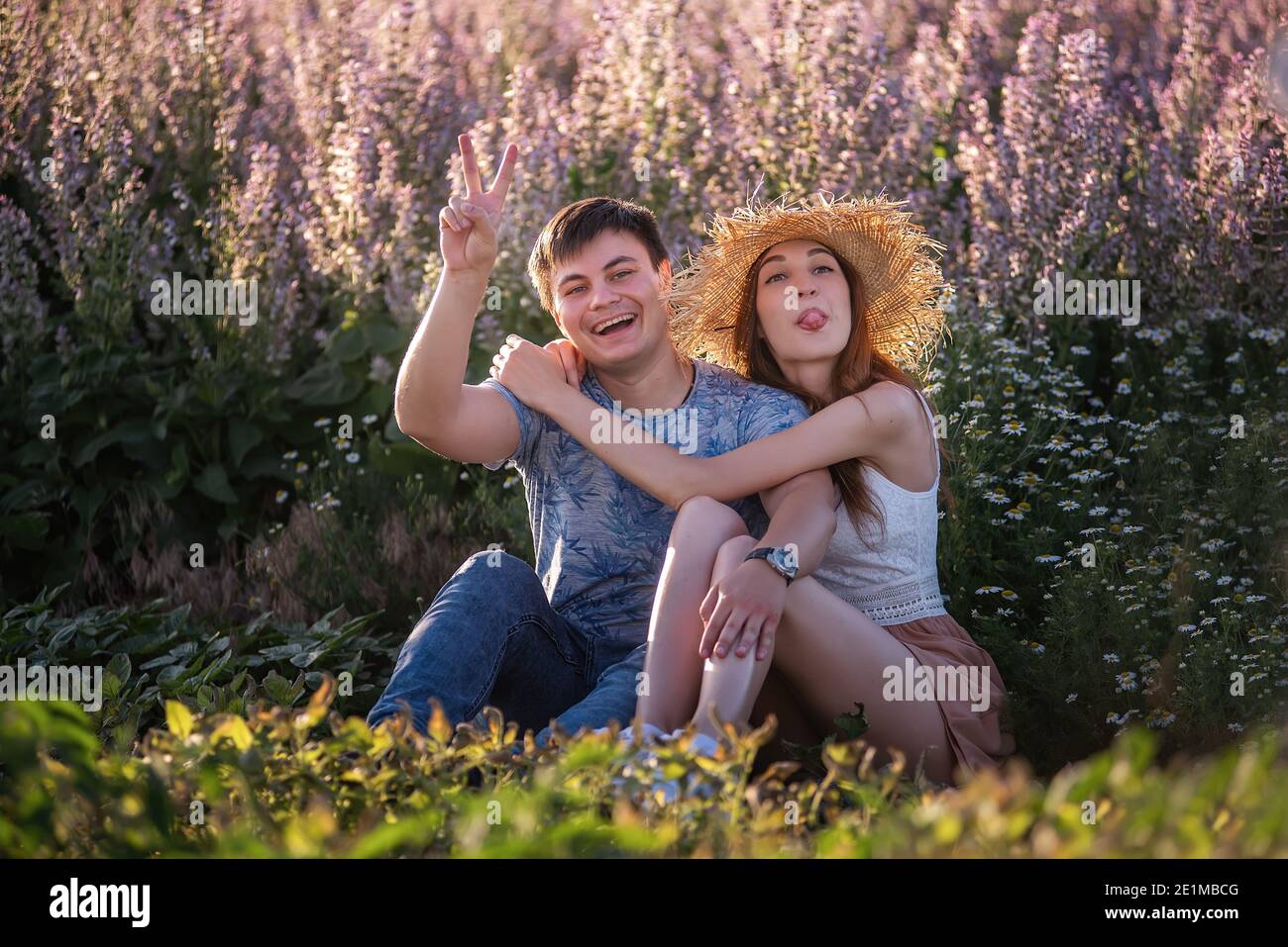 Couple heureux en amour s'enserre par le champ de sauge en fleur. Un jeune homme avec une belle fille en chapeau de paille s'amuse, se moque autour, agitant leur ha Banque D'Images