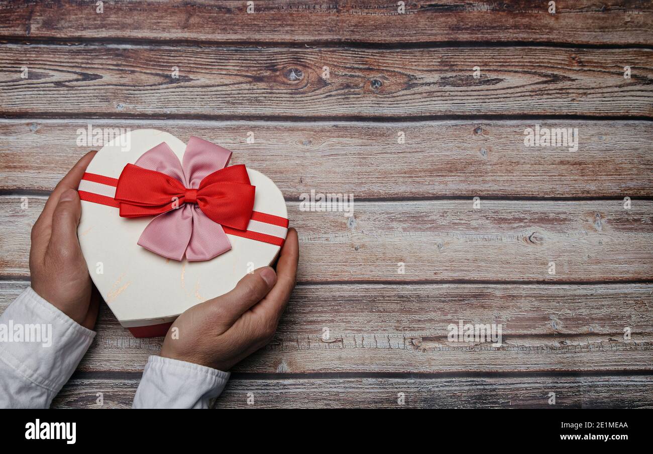 Mains de sexe masculin tenant une boîte cadeau en forme de coeur avec noeuds papillon. Thème de la Saint-Valentin. Concept LGTBI Banque D'Images