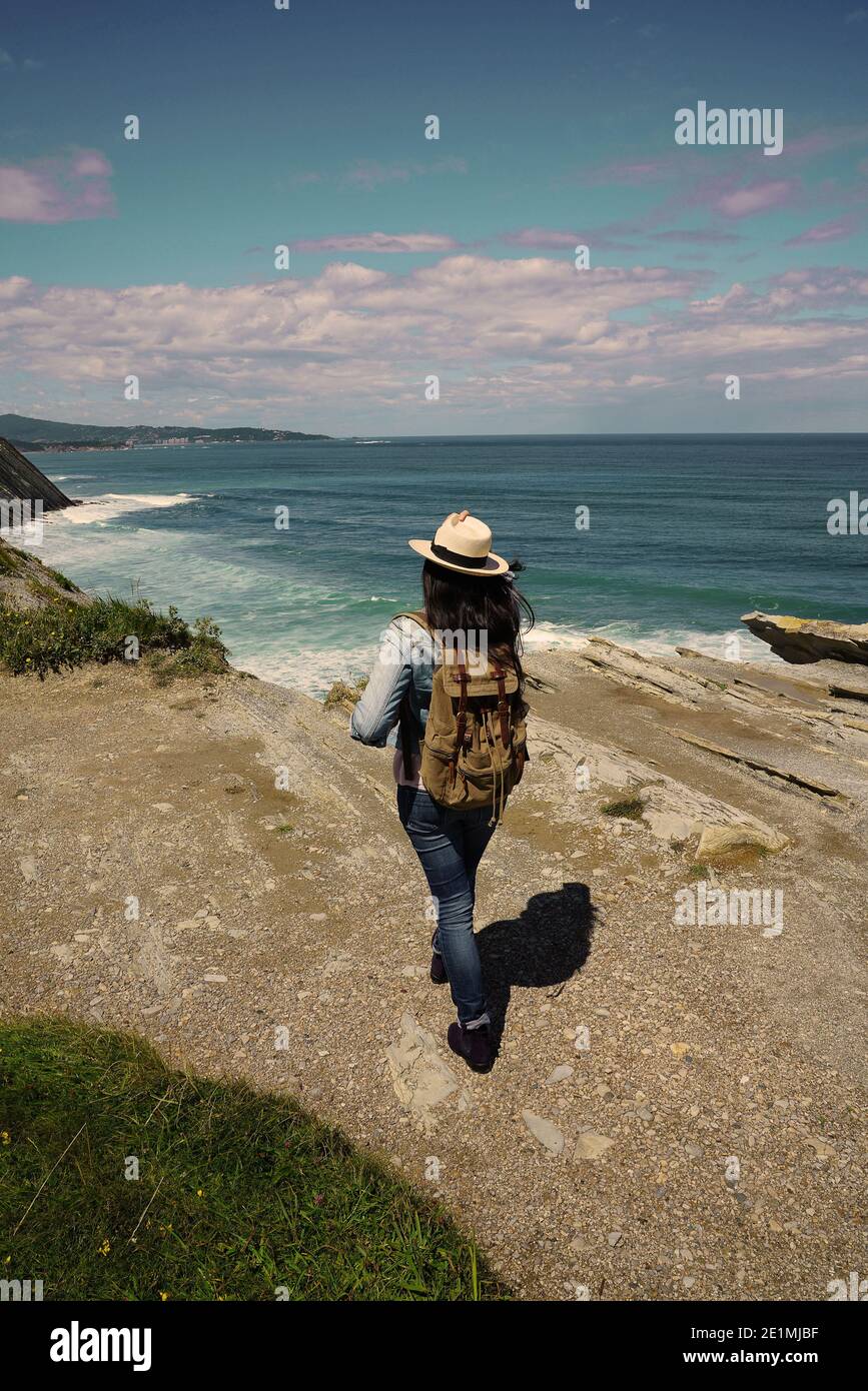 Femme avec chapeau marchant sur la côte de l'océan, en admirant le paysage Banque D'Images