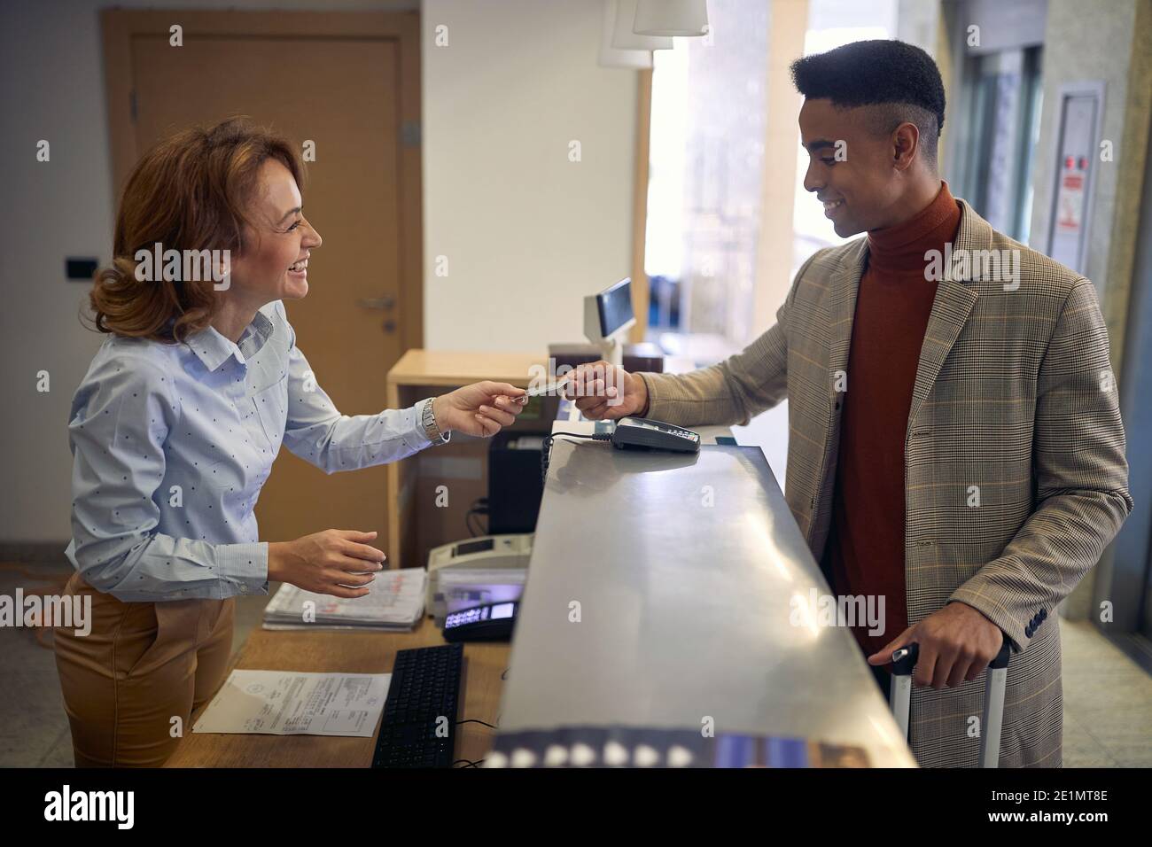 afro-american mâle payant avec carte à une femme amicale caucasienne réceptionniste Banque D'Images