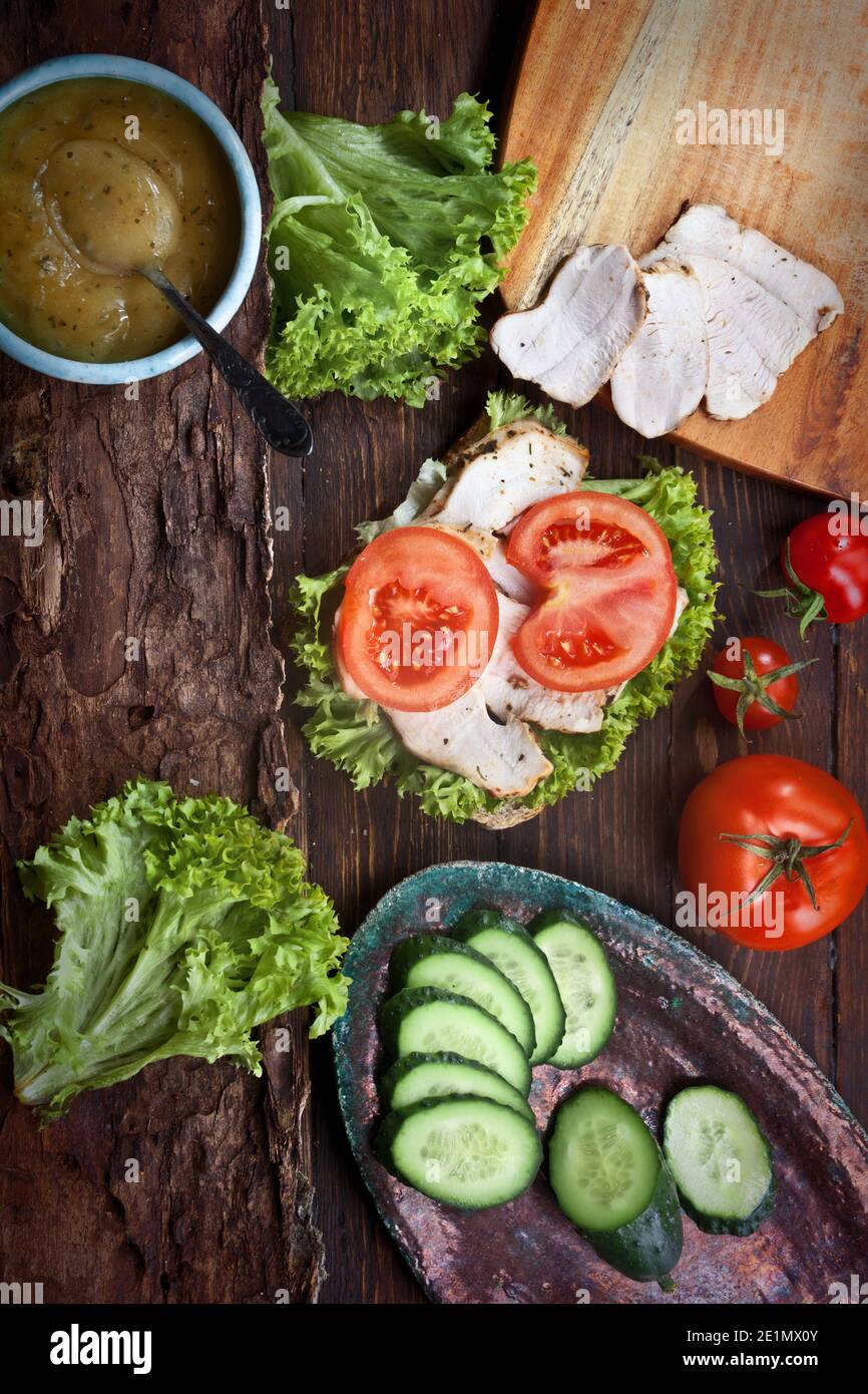 sandwich au bacon avec tomates fraîches, feuilles de salade de laitue, concombre et sauce, sur fond de table rustique en bois, personne Banque D'Images