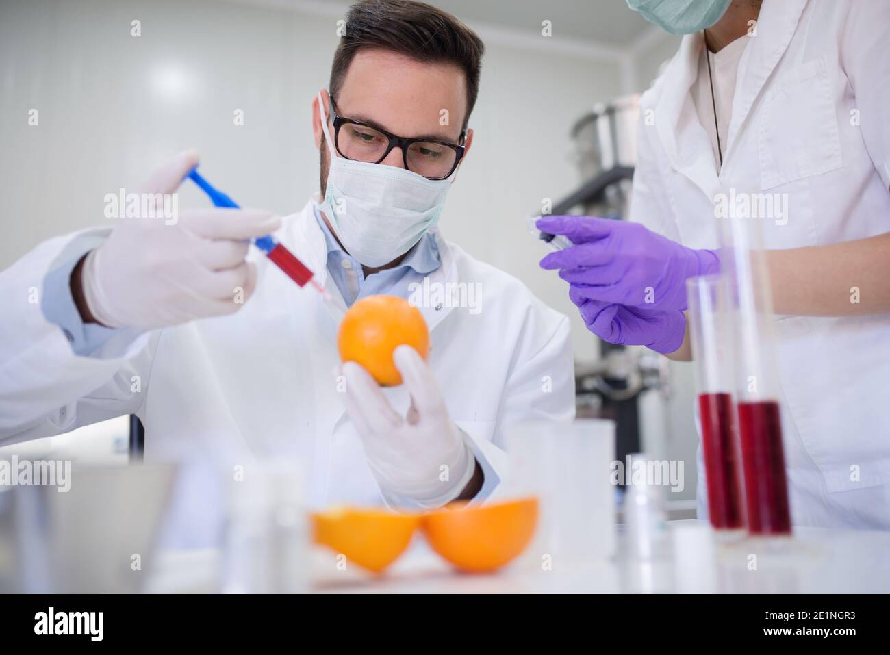 Le technologue injecte du liquide dans l'orange tandis que l'assistant l'aide. Banque D'Images