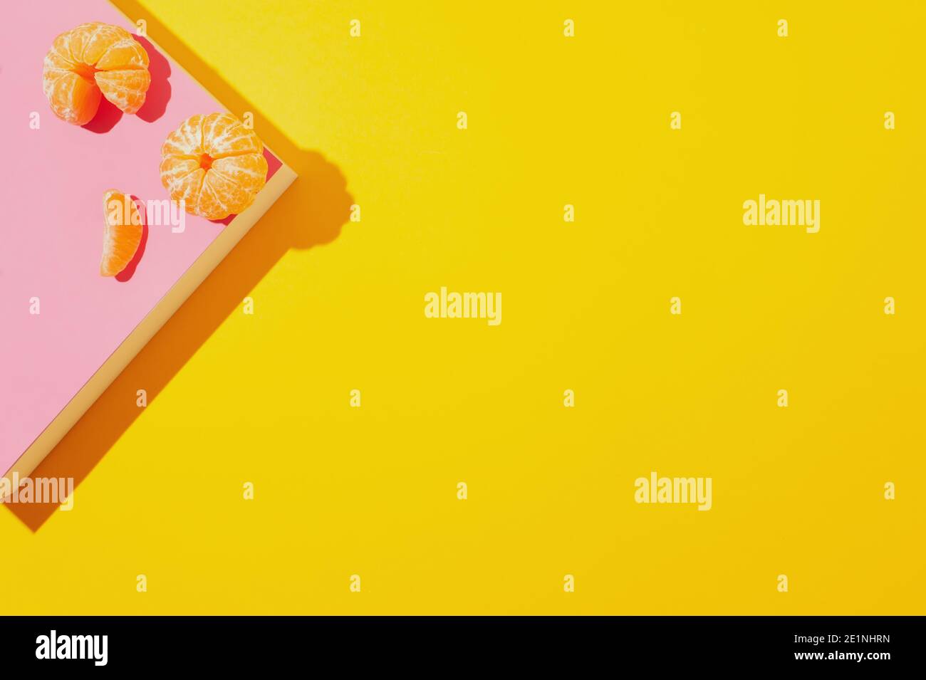 Mise en page créative avec des mandarines pelées sur un podium en papier rose sur fond jaune. Concept d'été abstrait. Image avec des ombres dures. Banque D'Images