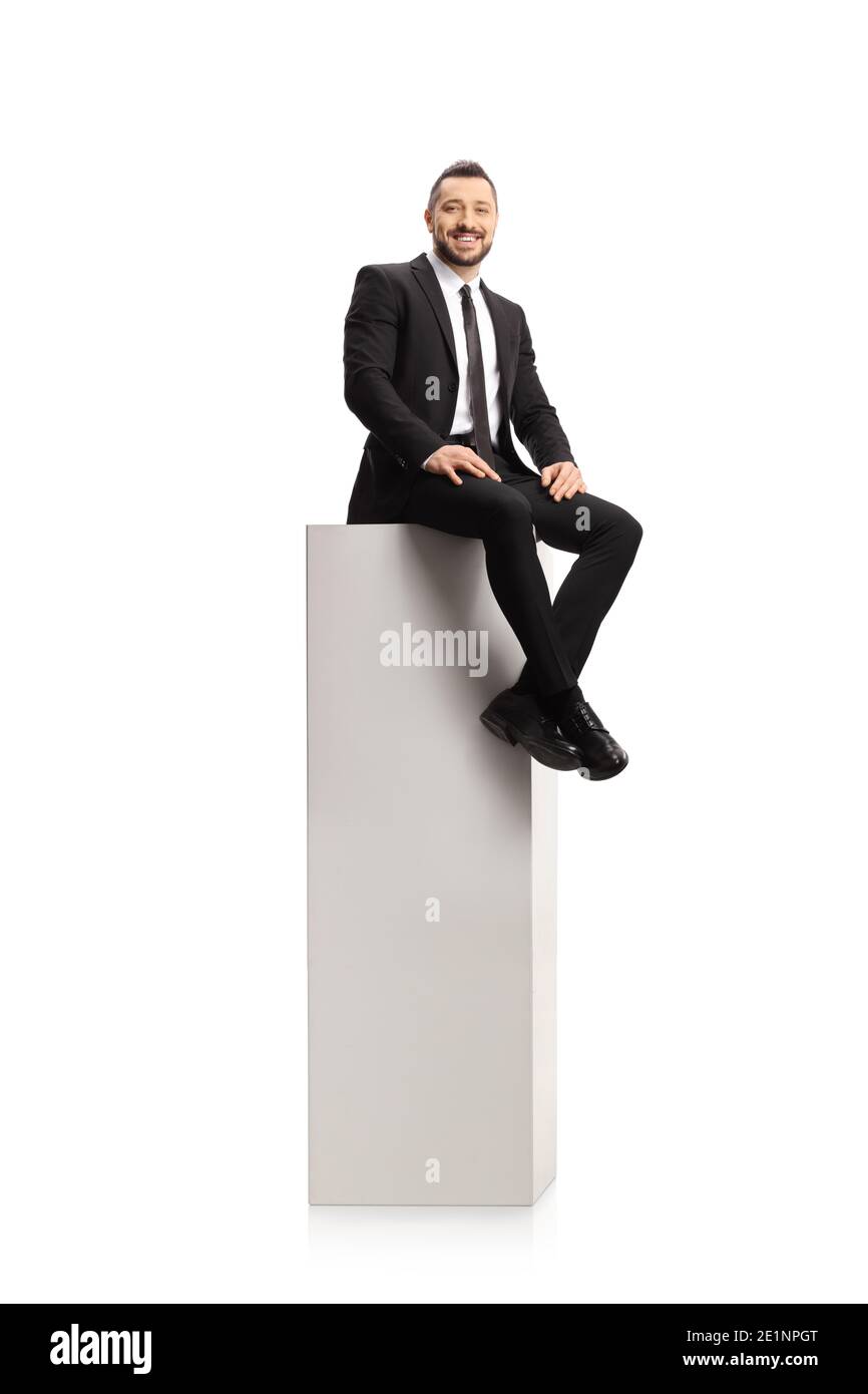 Homme en costume et cravate assis sur un grand colonne blanche et sourire à l'appareil photo isolé sur fond blanc Banque D'Images