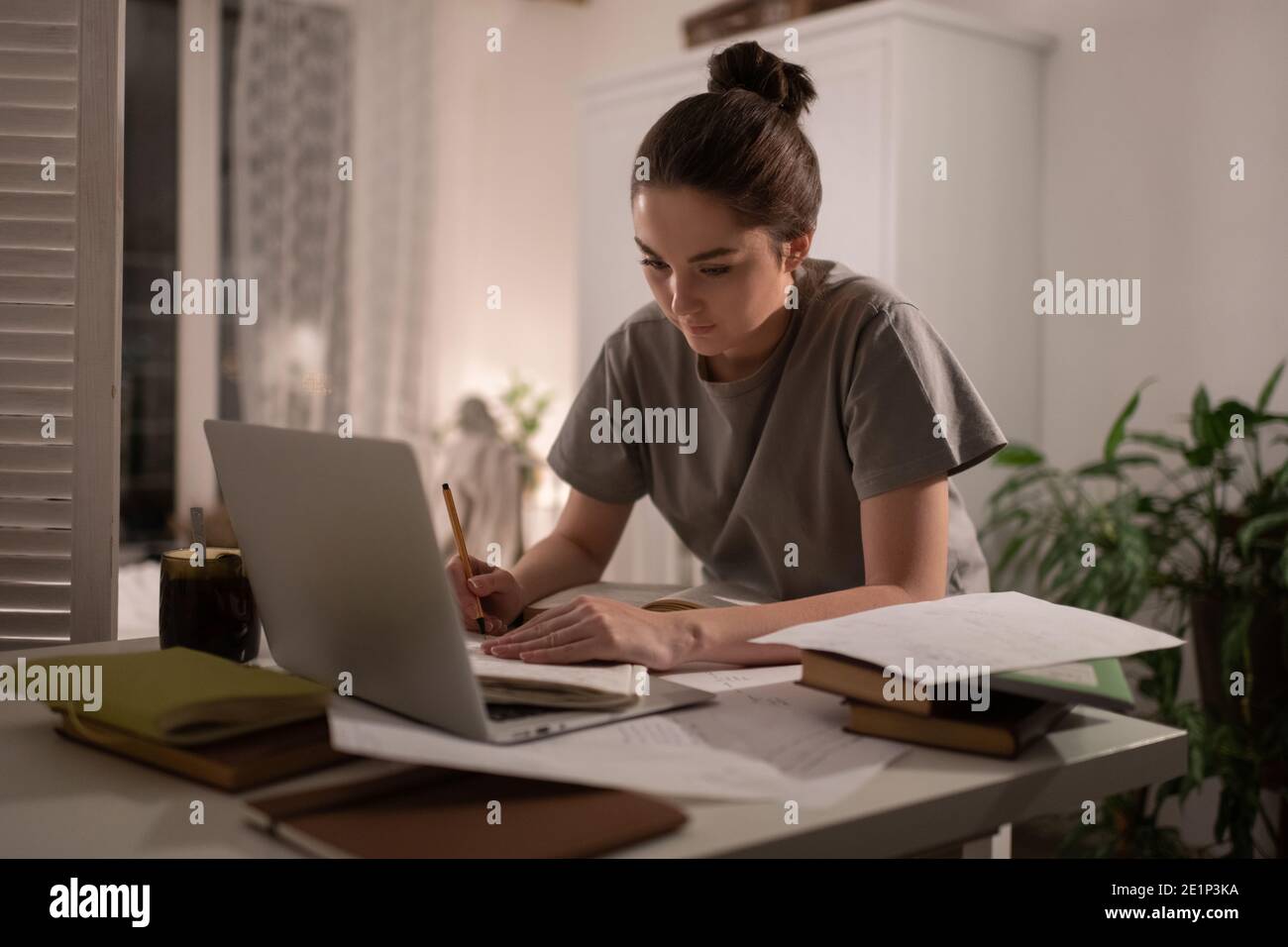 Femme intelligente prenant des notes lors de la préparation des examens en ligne à la table Banque D'Images