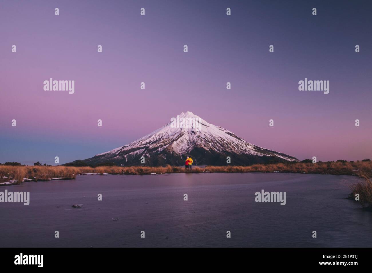 Jeune couple debout au pied du Mont Taranaki, au bord d'un lac gelé, en Nouvelle-Zélande Banque D'Images