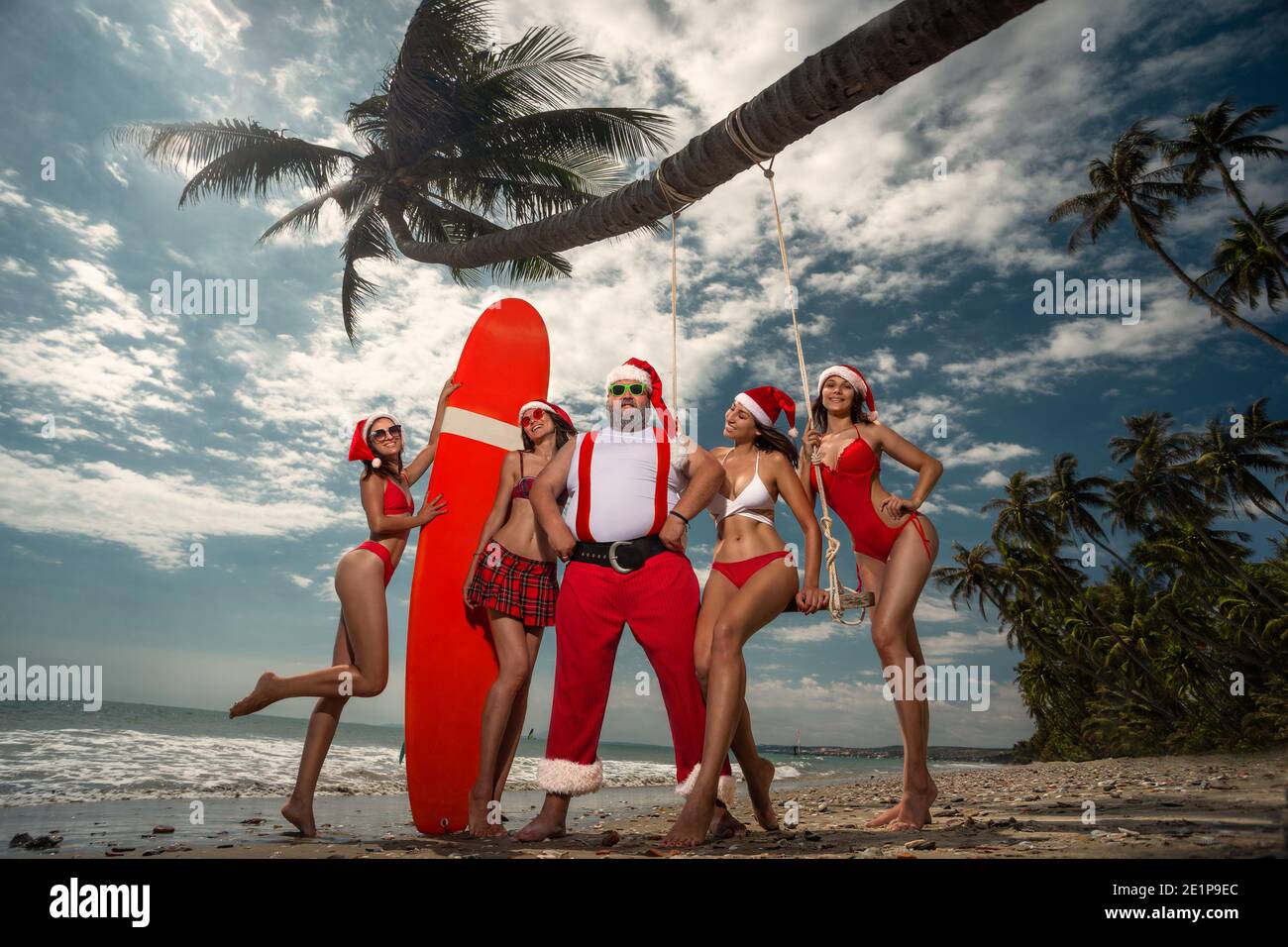 Noël Santa Claus se reposant sur la plage tropicale de sable de l'océan avec belles filles sexy Banque D'Images