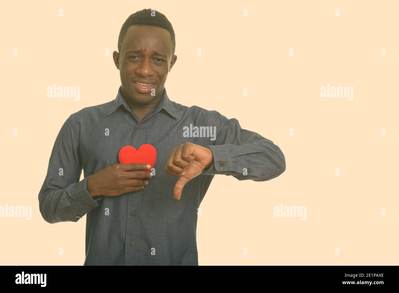 Sad Young African man holding cœur rouge sur la poitrine et giving thumb down Banque D'Images