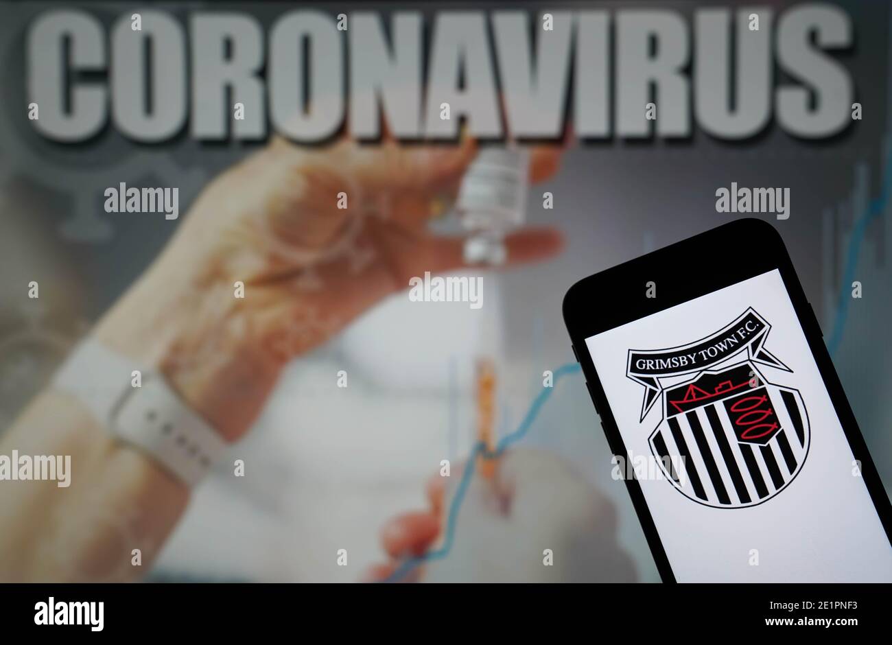 Le logo Grimsby Town football Club est visible sur un Téléphone portable avec une illustration du coronavirus sur un moniteur dans l'arrière-plan Banque D'Images