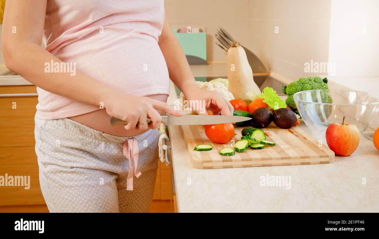 Gros plan de la femme enceinte yougn cuisine et coupe de tomates fraîches. Concept de mode de vie sain et de nutrition pendant la grossesse Banque D'Images
