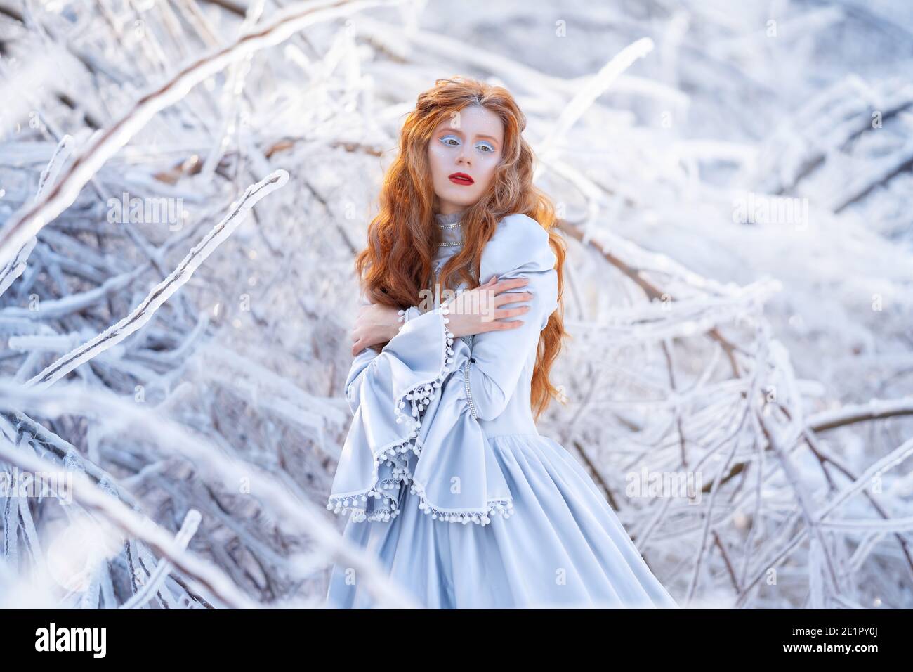 Une jeune femme à tête rouge, une princesse, marche dans une forêt d'hiver en robe bleue. Banque D'Images