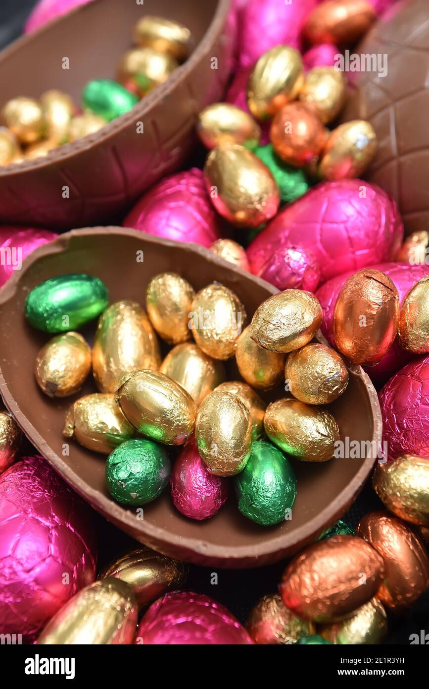 Pile ou groupe d'œufs de pâques au chocolat en feuilles colorées de différentes tailles, rose, rouge, or et vert lime, en deux moitiés. Banque D'Images