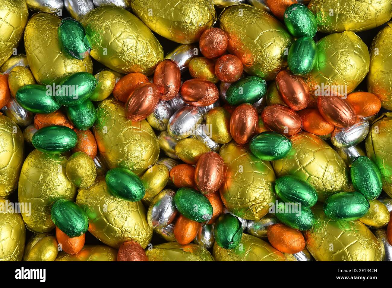 Petits et grands jaunes, or, orange, vert et argent couleurs printanières d'œufs de pâques au chocolat enveloppés de papier d'aluminium, sur fond noir. Banque D'Images