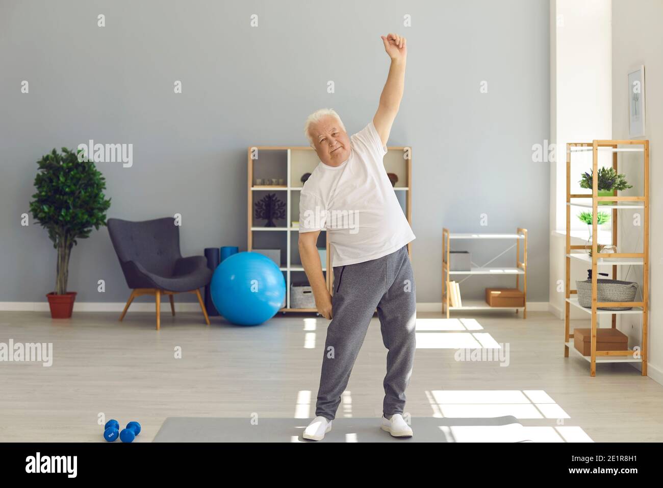 Homme mature positif à la maison sportswear faire des exercices légers à la maison ou dans un centre de réadaptation. Banque D'Images