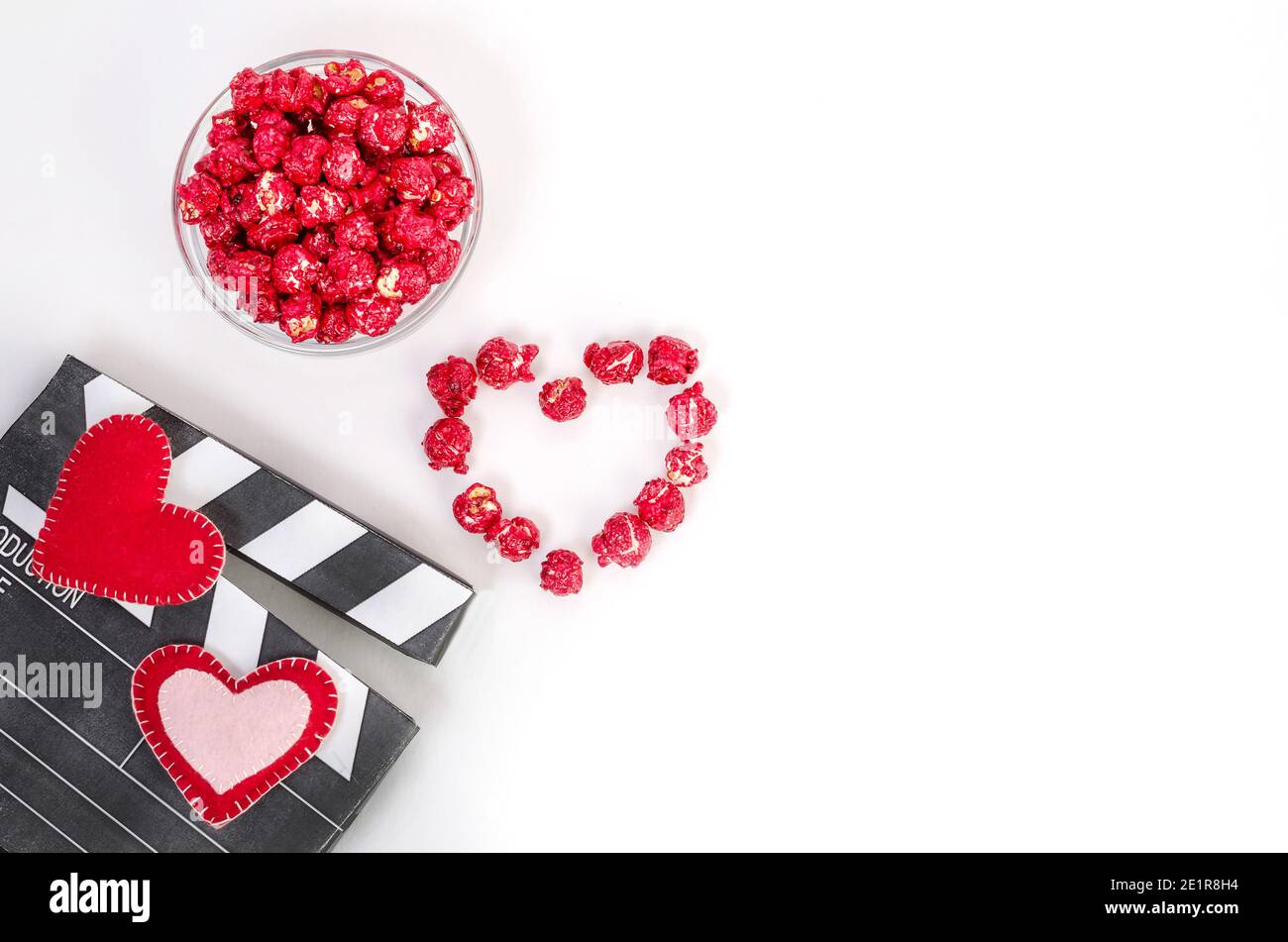 Concept de film de la Saint-Valentin. Papperboard aux coeurs, pop-corn au caramel rouge avec espace pour les copies sur fond blanc. Banque D'Images