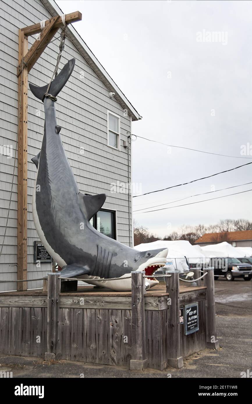 Une réplique d'un requin suspendu sur un quai se trouve devant un magasin sur le côté de l'autoroute près de Salisbury Beach, Massachusetts, sur un evenin couvert Banque D'Images