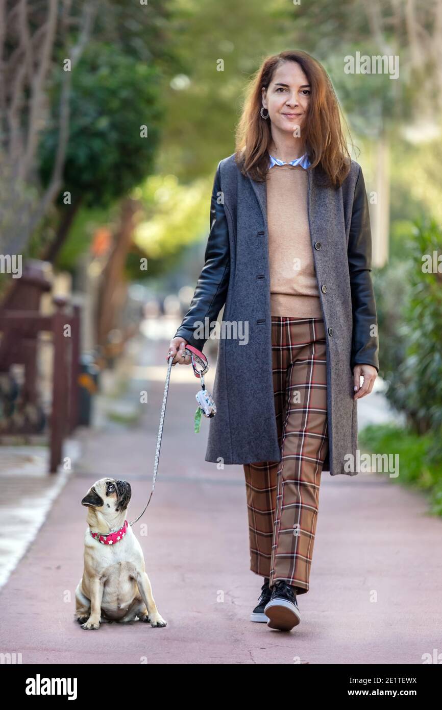 Une femme portant un manteau marchant avec son chien pug sur un trottoir, à l'extérieur Banque D'Images