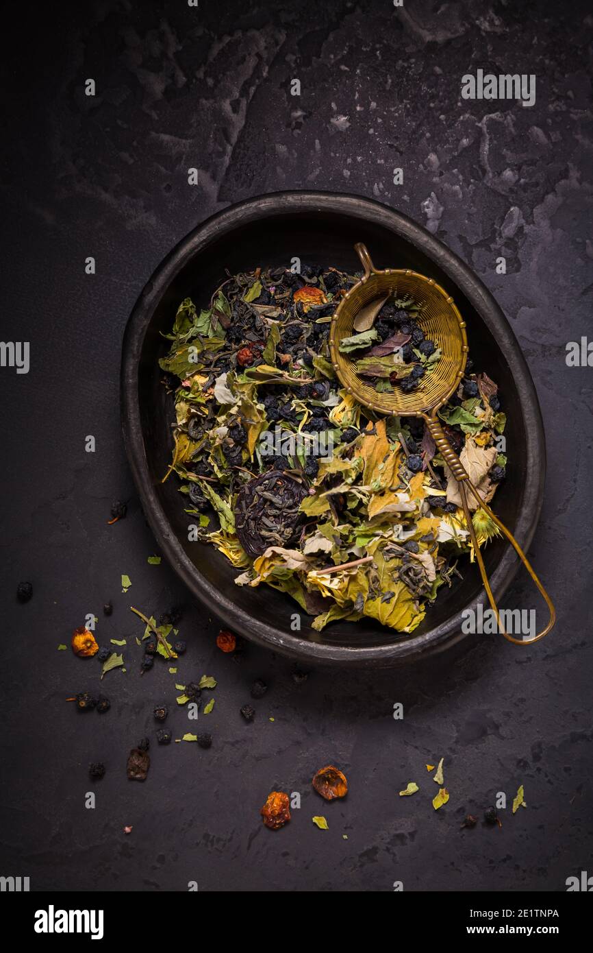 Mélange de thés, d'herbes de thé biologique séchées et de fruits dans un bol avec passoire à thé sur fond noir Banque D'Images