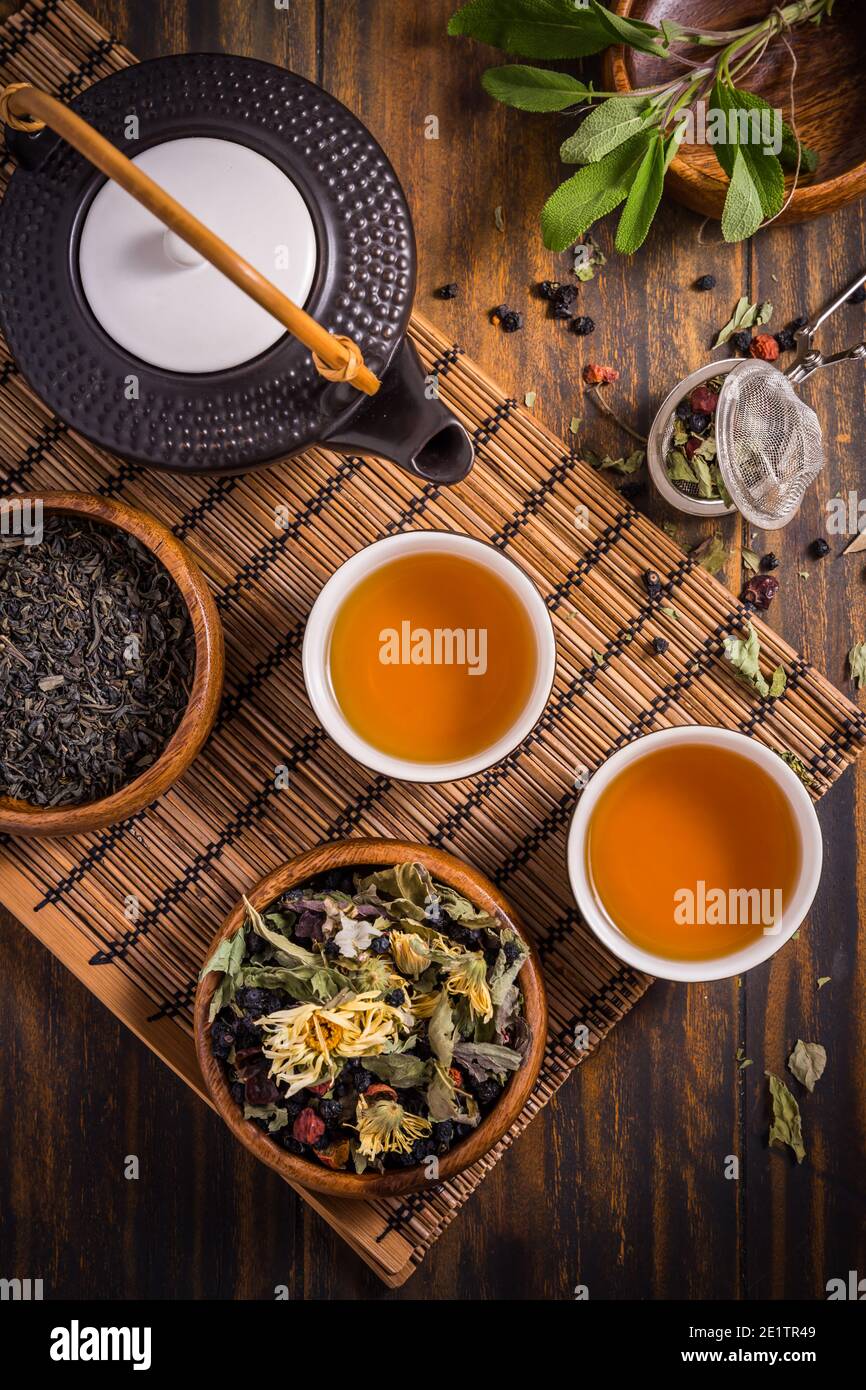 Concept de tisane et de fruit avec théière et infuser et feuilles de plantes assorties sur fond en bois Banque D'Images