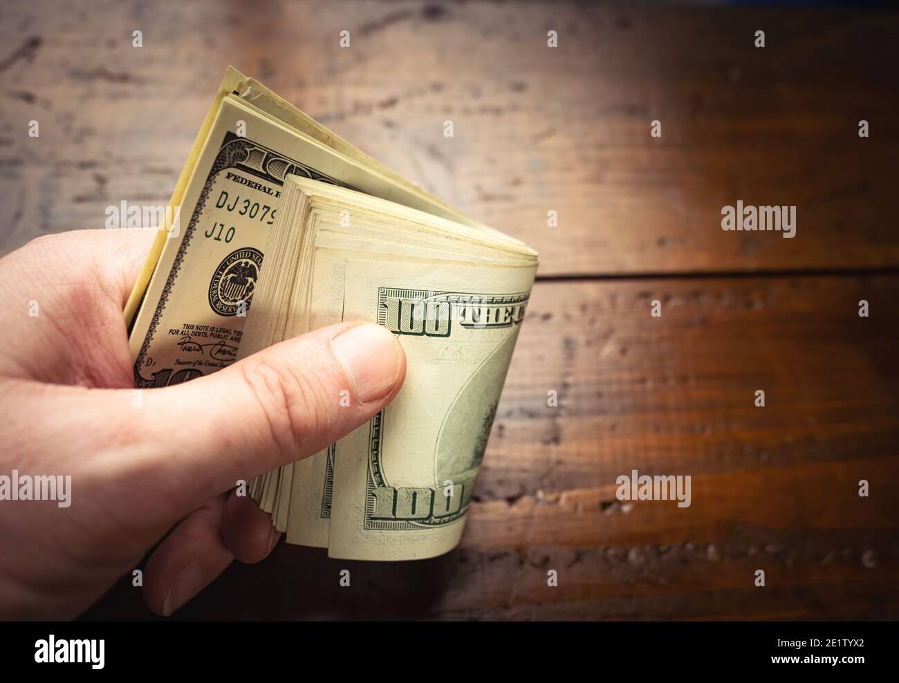 Main tenant cent billets américains sur fond de table en bois. Espèces de billets de cent dollars, monnaie papier. Banque D'Images