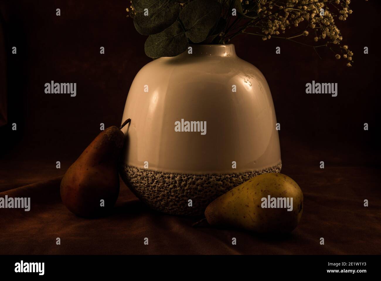 Vase blanc doux avec fleurs « Baby's Breath » sur fond sombre, les fruits artificiels ajoutent une touche agréable. Banque D'Images