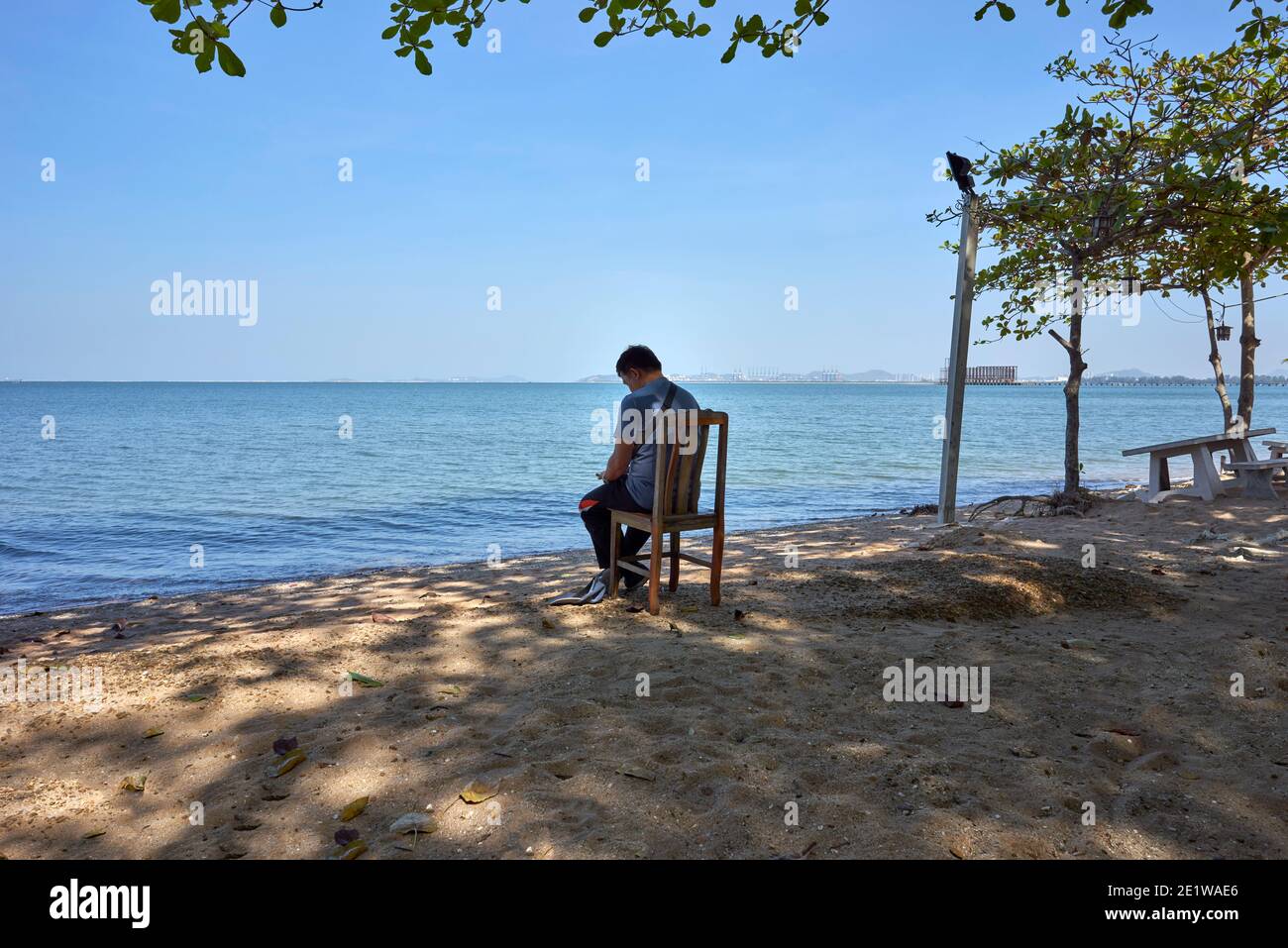 Homme solitaire assis sur une chaise relaxant à l'extérieur à la plage et vue sur l'océan en Thaïlande Asie du Sud-est Banque D'Images