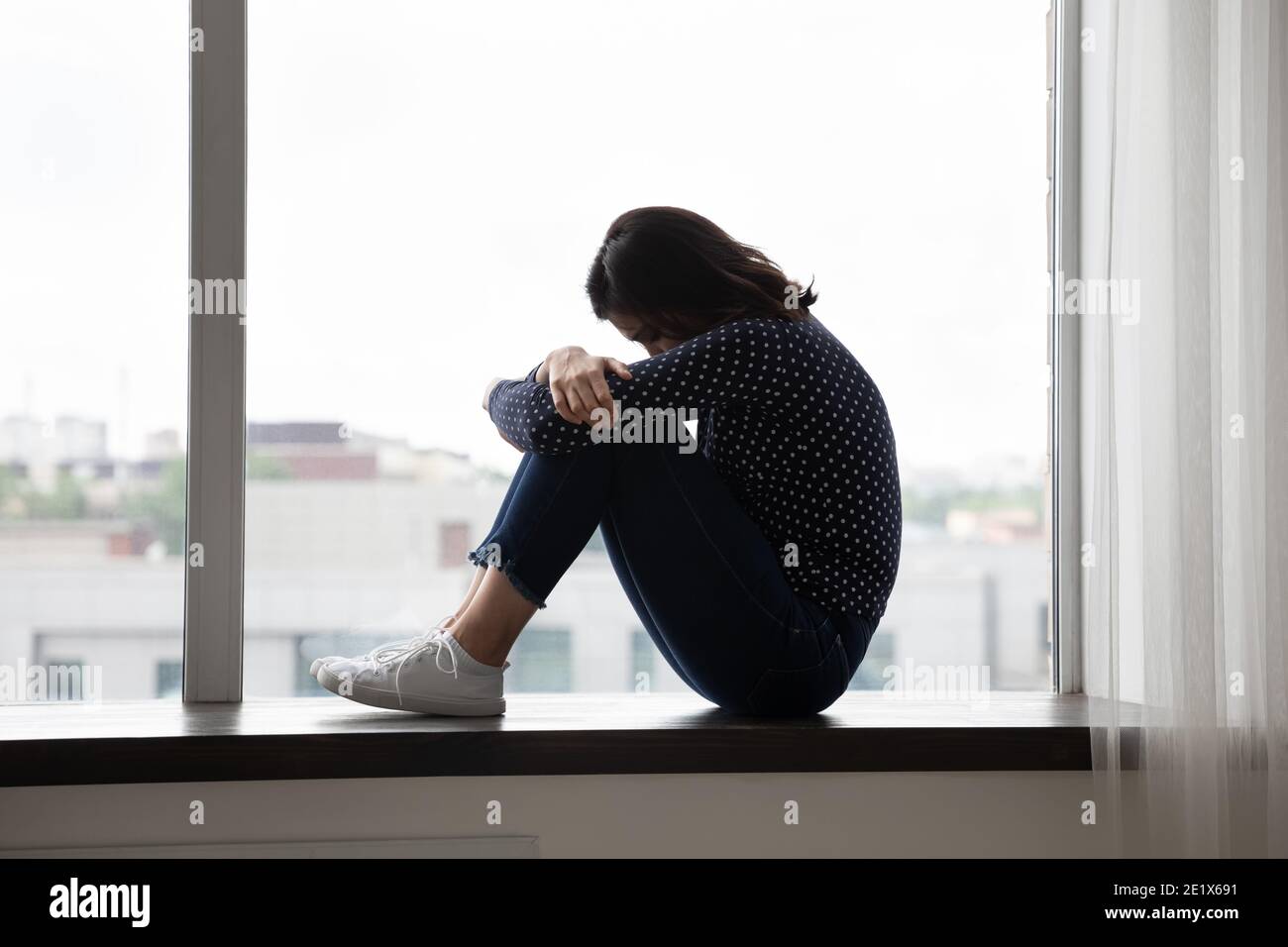Une femme asiatique désespérée et malheureuse assise sur un rebord de fenêtre. Banque D'Images