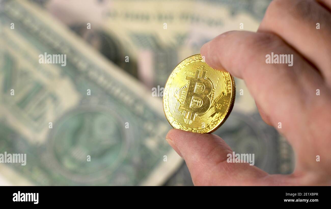 Tenez une pièce en bitcoin d'or sur un arrière-plan flou de nombreuses pièces d'or. Doigts d'un homme tenant Bitcoin, pièce d'or Banque D'Images