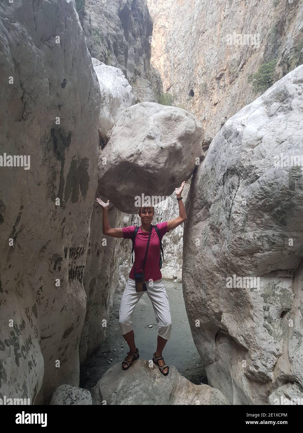 Fille se tient dans une partie étroite du canyon et, comme elle l'était, tient une énorme pierre. Canyon Saklikent en Turquie. Banque D'Images