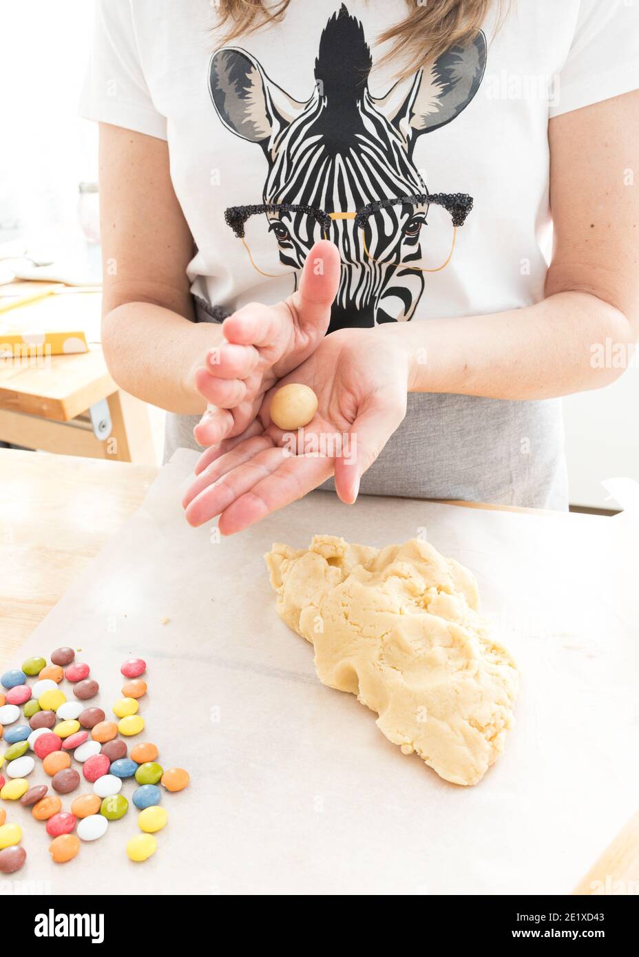 Femme vêtue d'un t-shirt zébré qui forme un morceau de pâte. Plusieurs bonbons au chocolat et une grande quantité de pâte sont sur la table. Banque D'Images