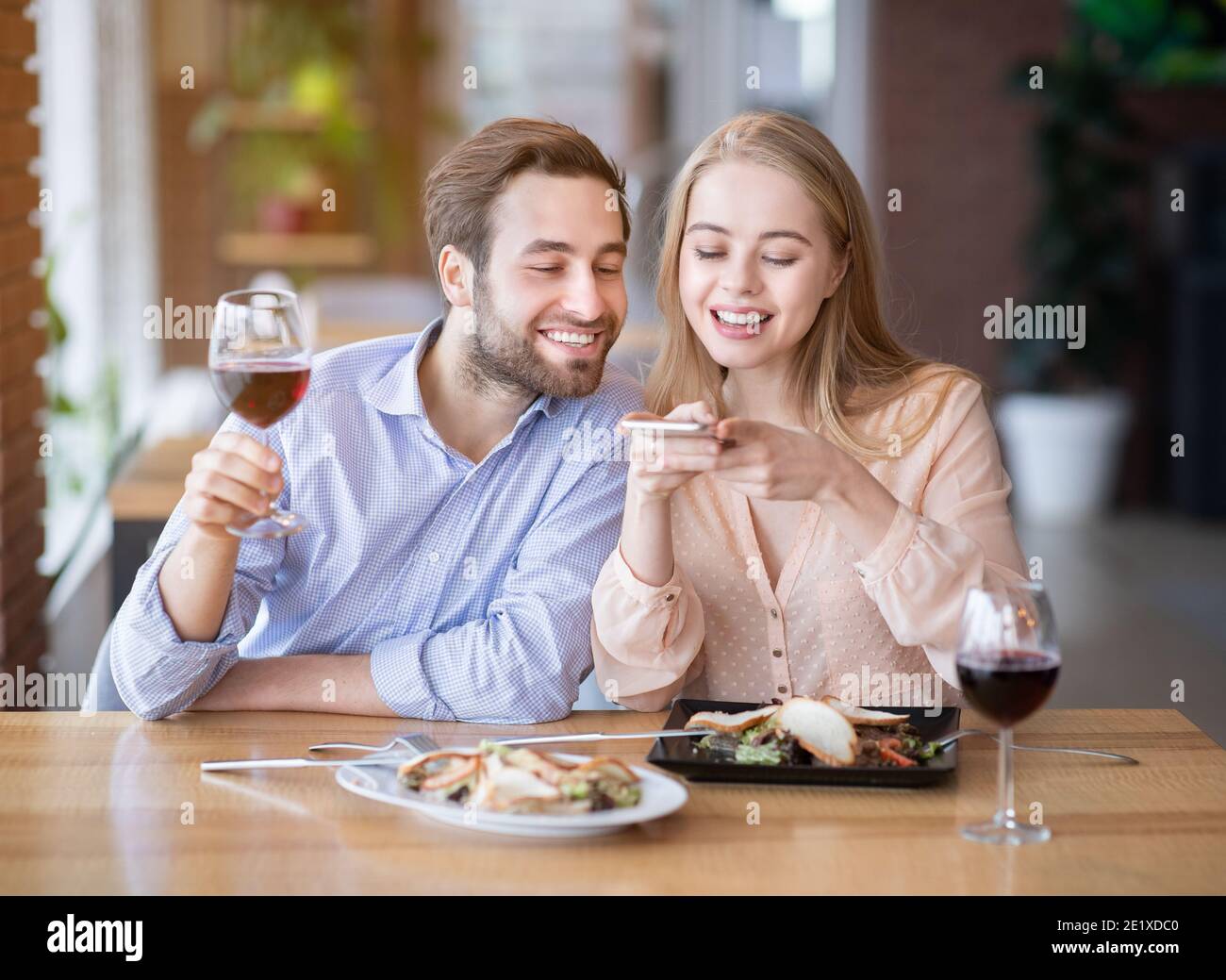 Couple millénaire affectueux prenant des photos de mets délicieux et de vin sur smartphone au restaurant Banque D'Images