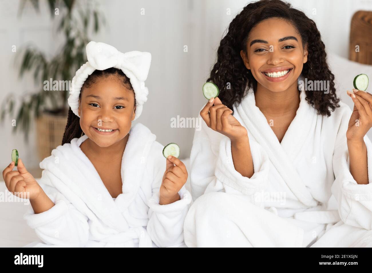 Spa a la maison. Belle mere africaine et fille dans des peignoirs contenant des tranches de concombre Photo Stock Alamy