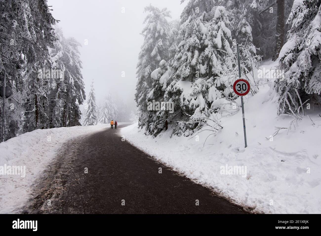 Longue route en paysage d'hiver avec panneau de signalisation indiquant la limite de vitesse et deux personnes à pied Banque D'Images