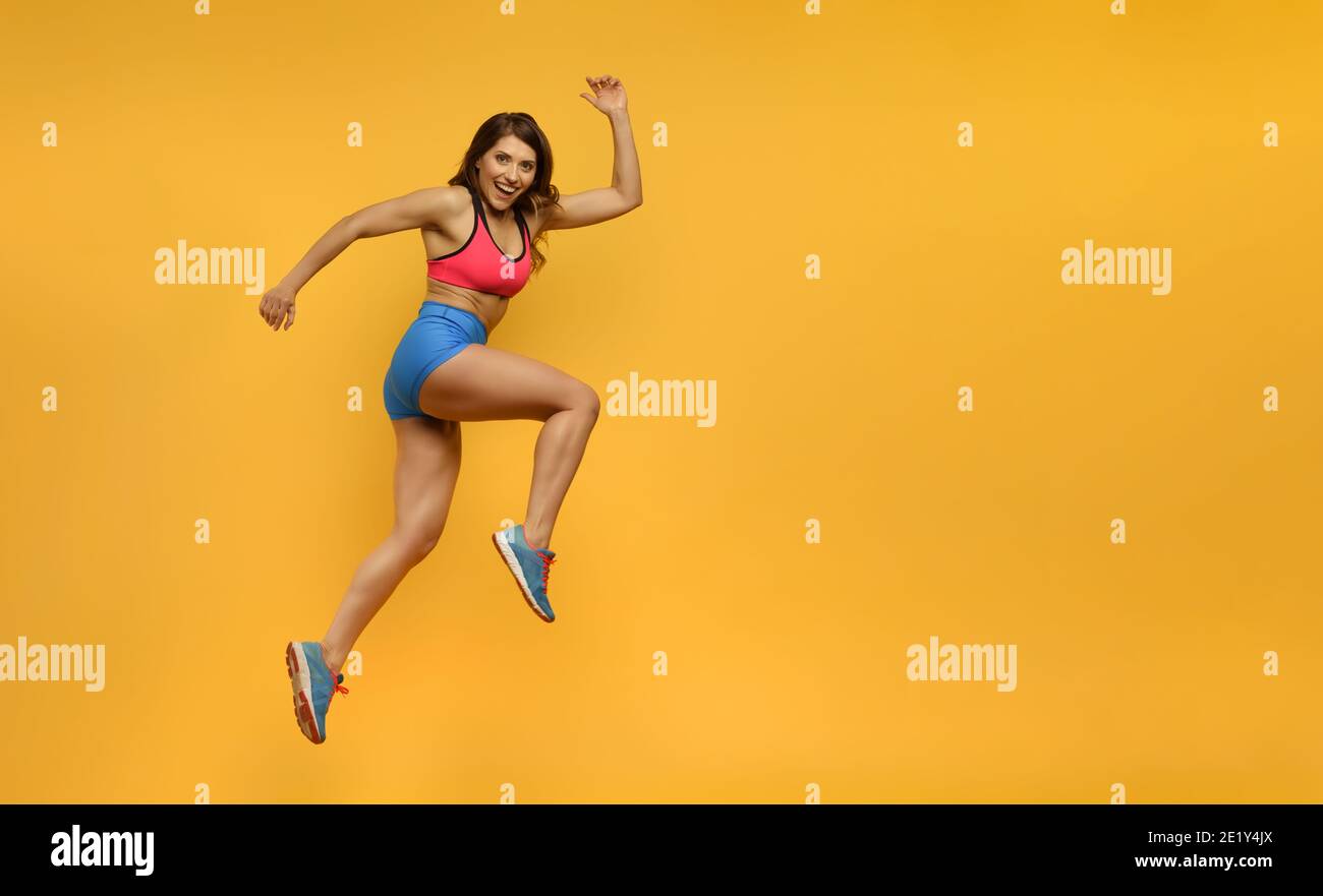 La femme sportive court sur fond jaune. Expression heureuse et joyeuse. Banque D'Images