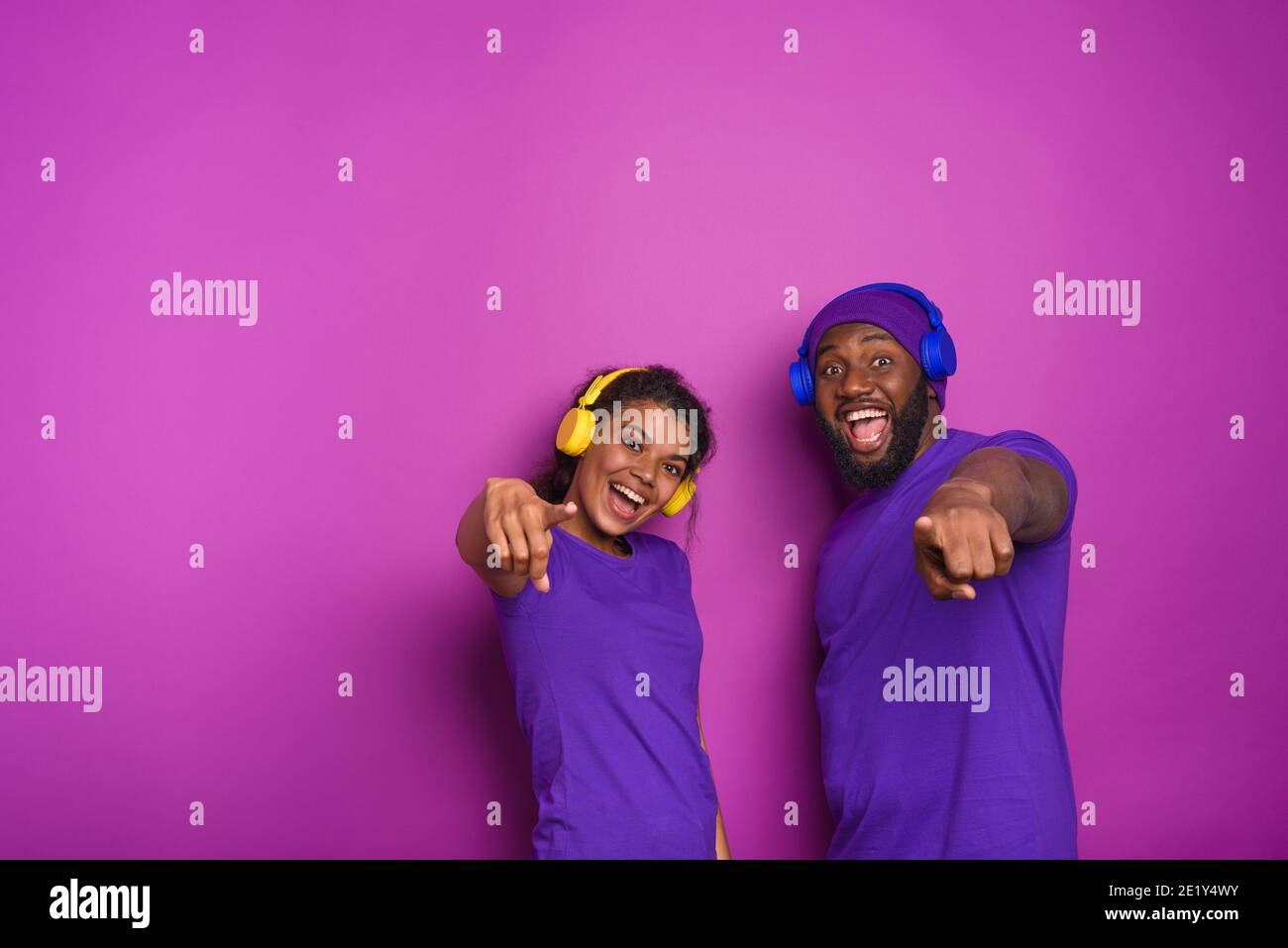 Couple avec casque écouter de la musique et avoir l'expression surprise. Arrière-plan violet Banque D'Images