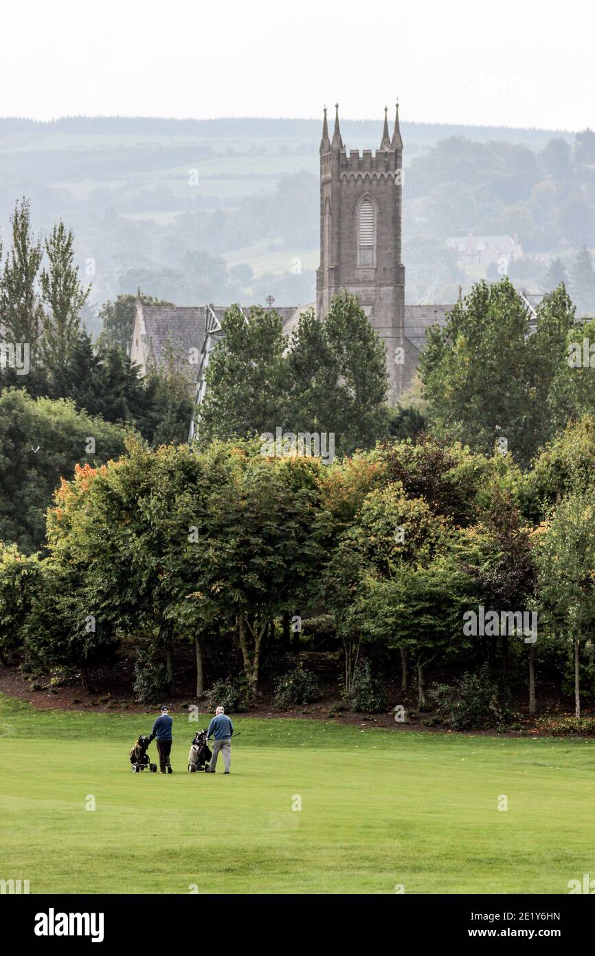 Deux hommes jouant au golf sur le parcours Citywest Hotel Golf Club avec l'église de la Nativité de la Sainte Vierge Marie en arrière-plan. Dublin, Irlande. Banque D'Images