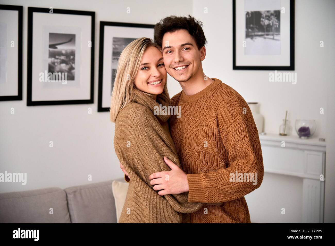 Un jeune couple heureux qui se tient debout en regardant l'appareil photo à la maison, portrait. Banque D'Images