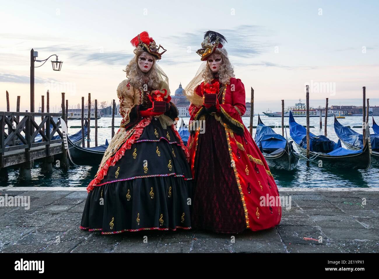 Deux femmes vêtues de costumes traditionnels décorés et de masques peints pendant le carnaval de Venise avec le monastère de San Giorgio derrière Venise, en Italie Banque D'Images