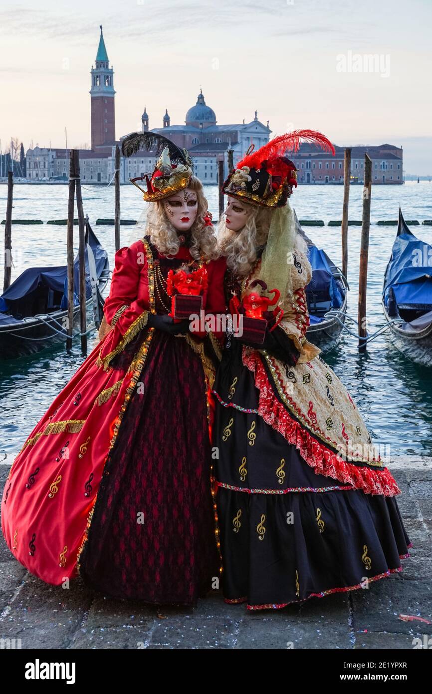 Deux femmes vêtues de costumes traditionnels décorés et de masques peints pendant le carnaval de Venise avec le monastère de San Giorgio derrière Venise, en Italie Banque D'Images