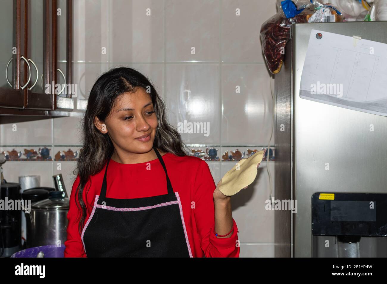 jeune femme portant une chemise rouge préparant des tortillas avec ses mains sur sa maison de cuisine Banque D'Images