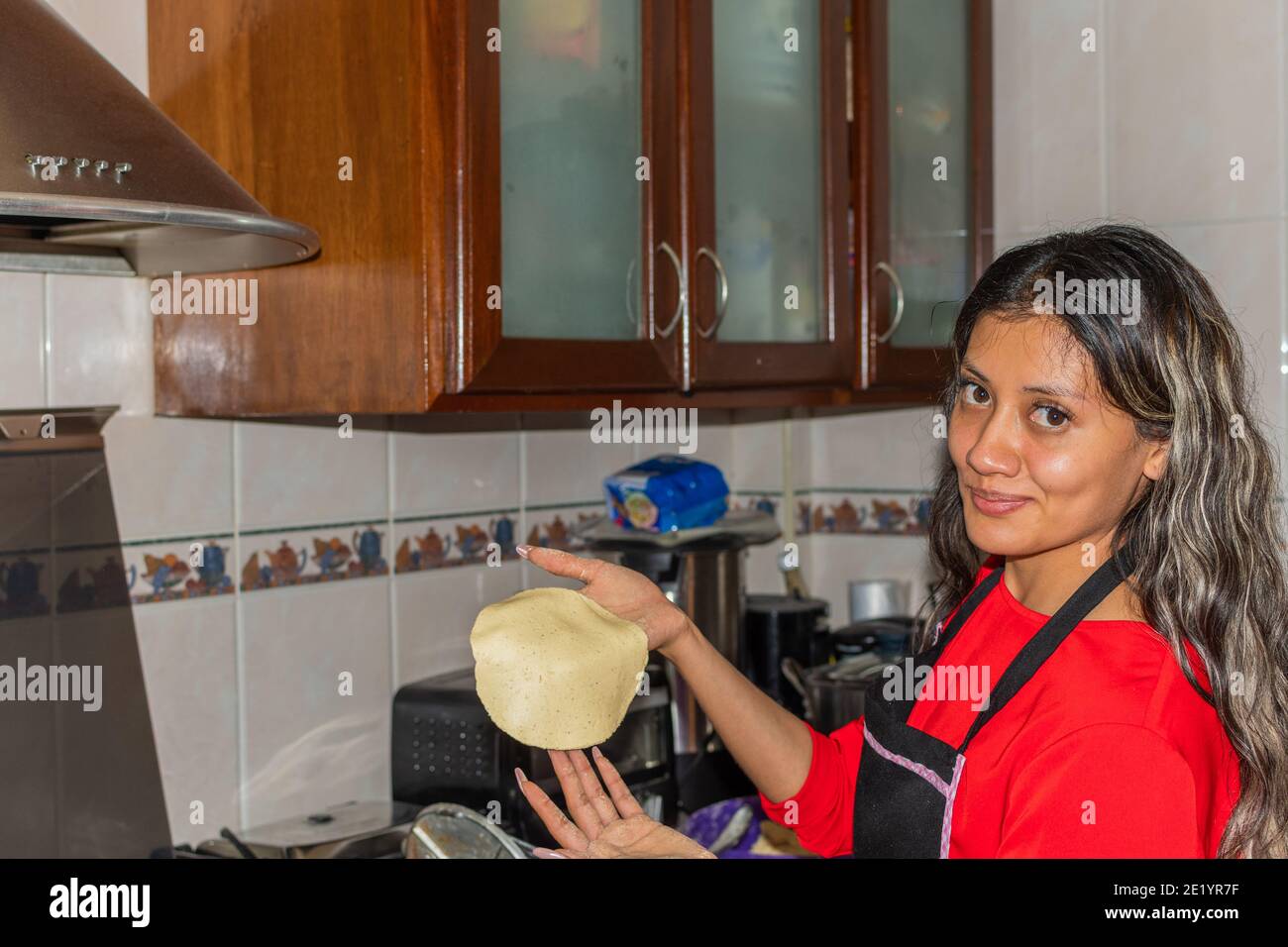 jeune femme portant une chemise rouge préparant des tortillas avec ses mains sur sa maison de cuisine Banque D'Images