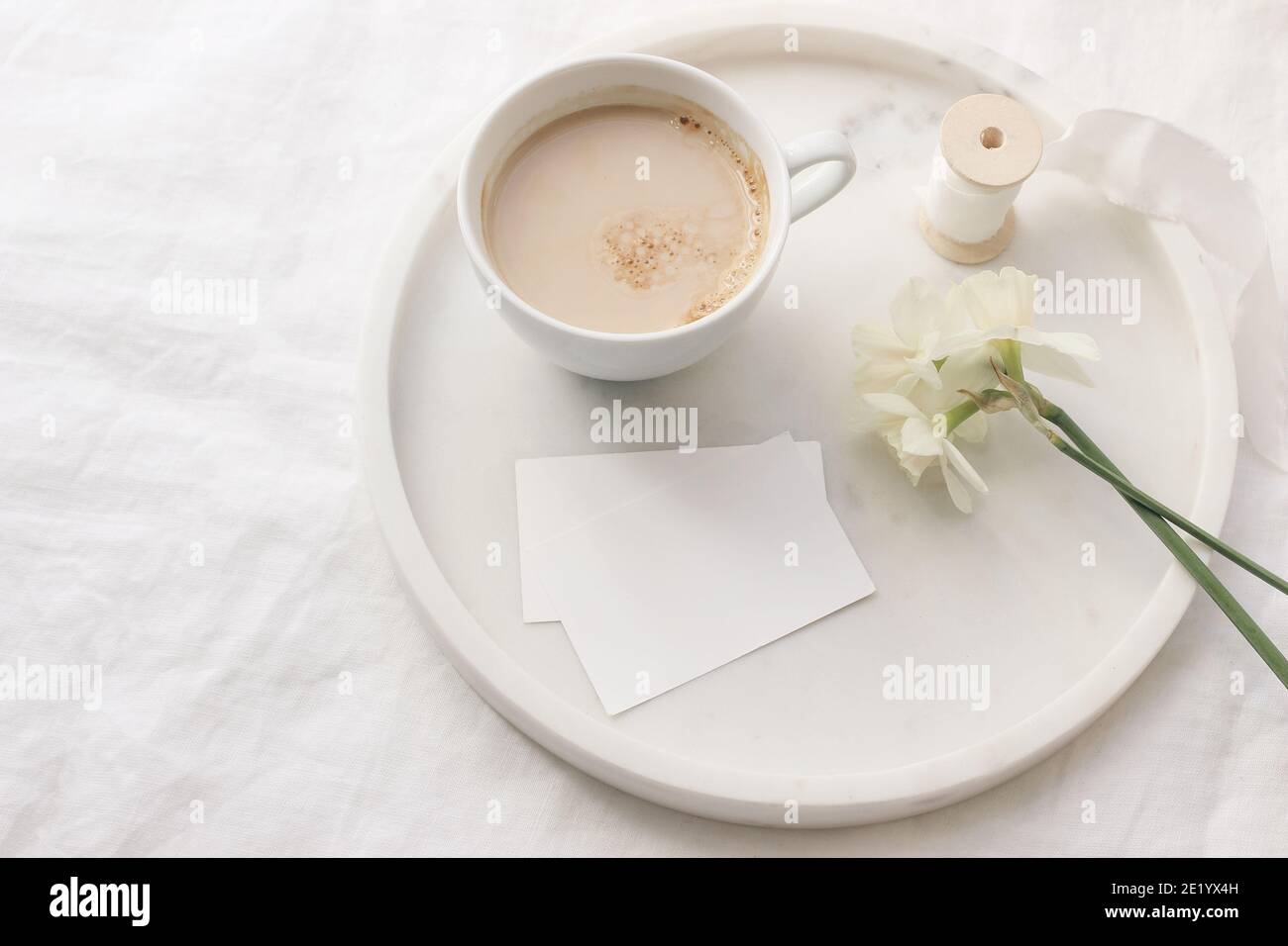 Mariage de printemps encore la vie. Maquettes de cartes de visite. Ruban de soie, narcisse jonquilles fleurs sur plateau en marbre. Tasse de café avec lait. Table en lin blanc Banque D'Images