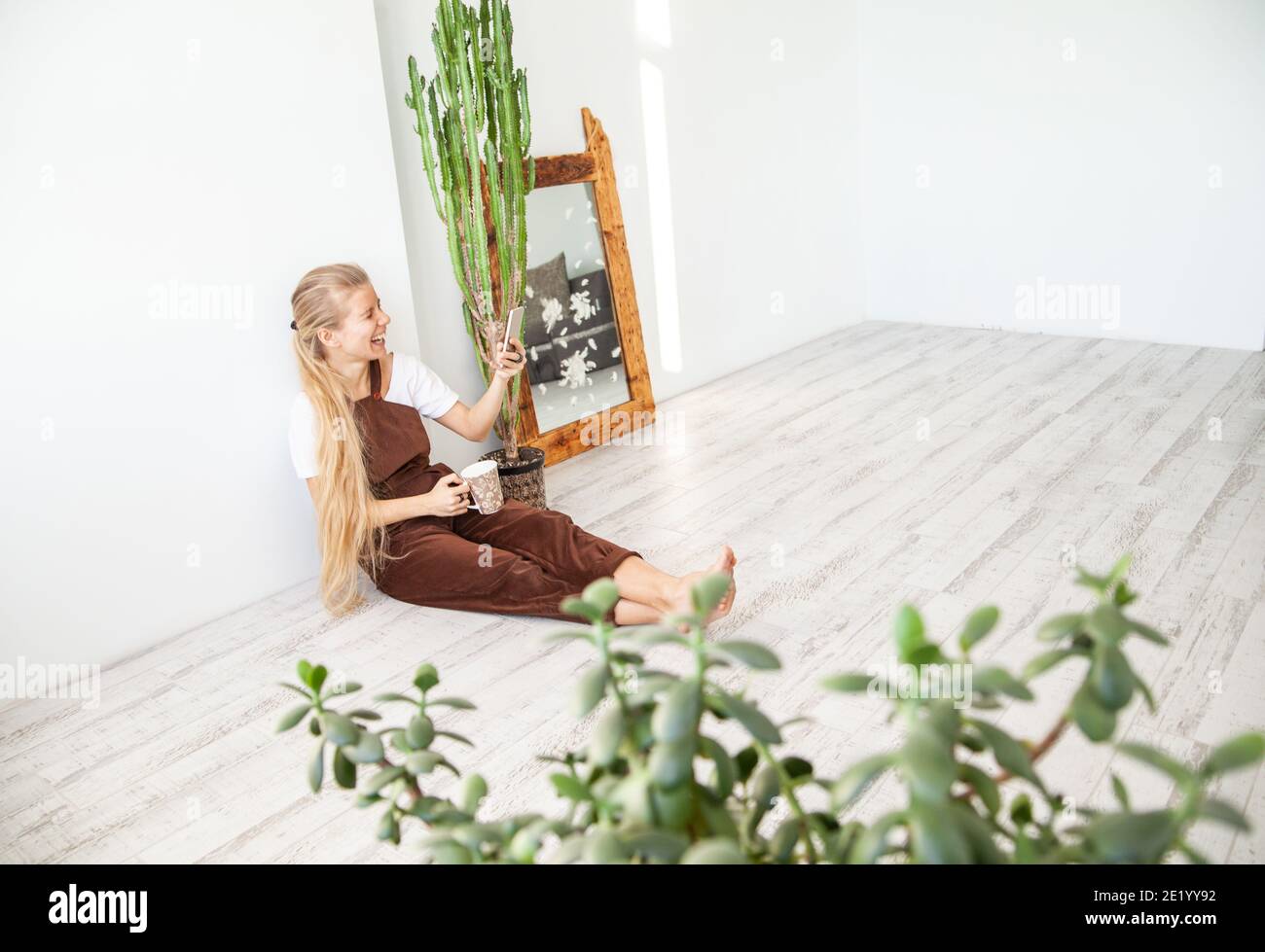 Jeune femme joyeuse avec mug à l'aide d'un smartphone Banque D'Images