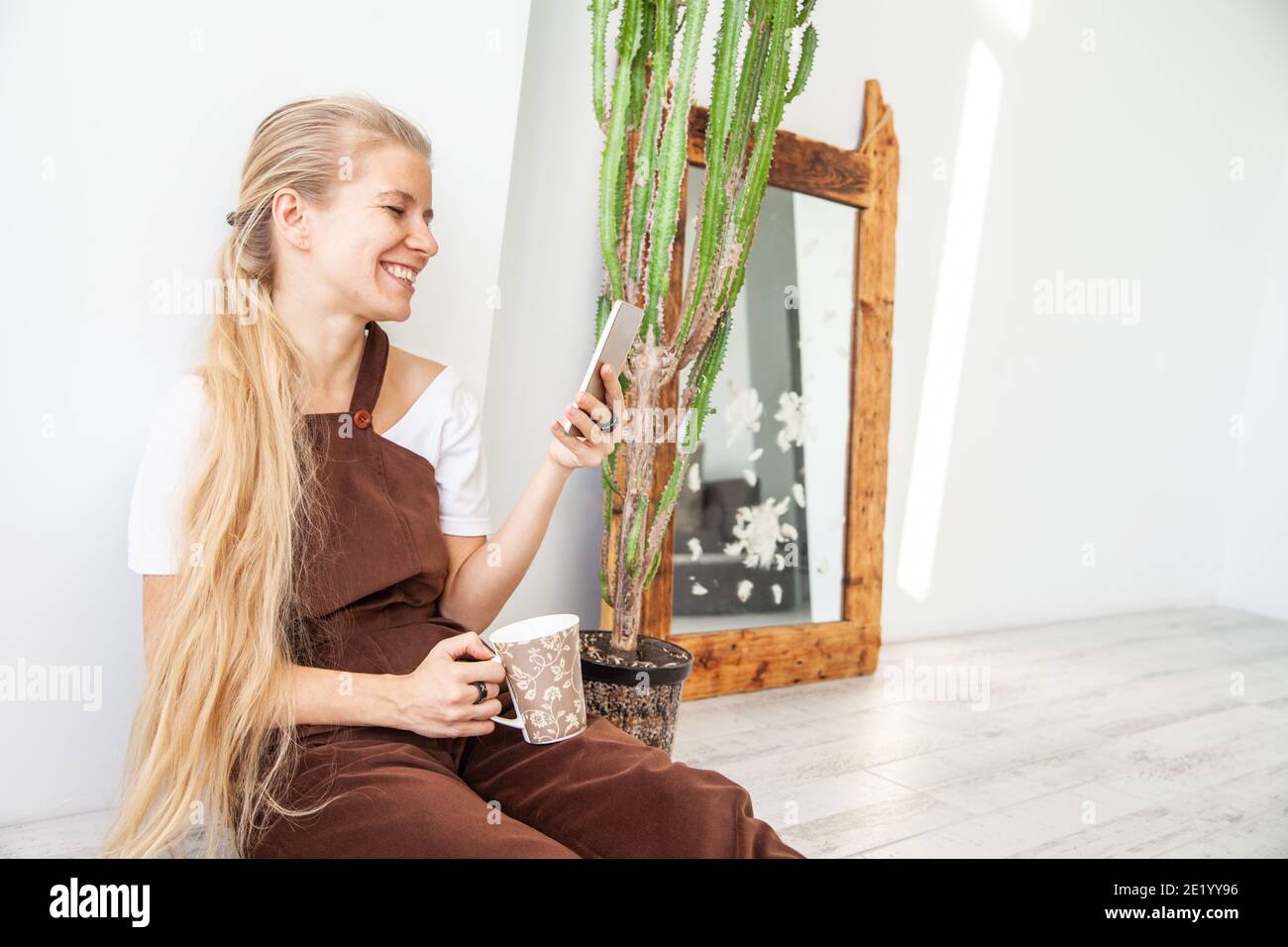 Jeune femme joyeuse avec mug à l'aide d'un smartphone Banque D'Images