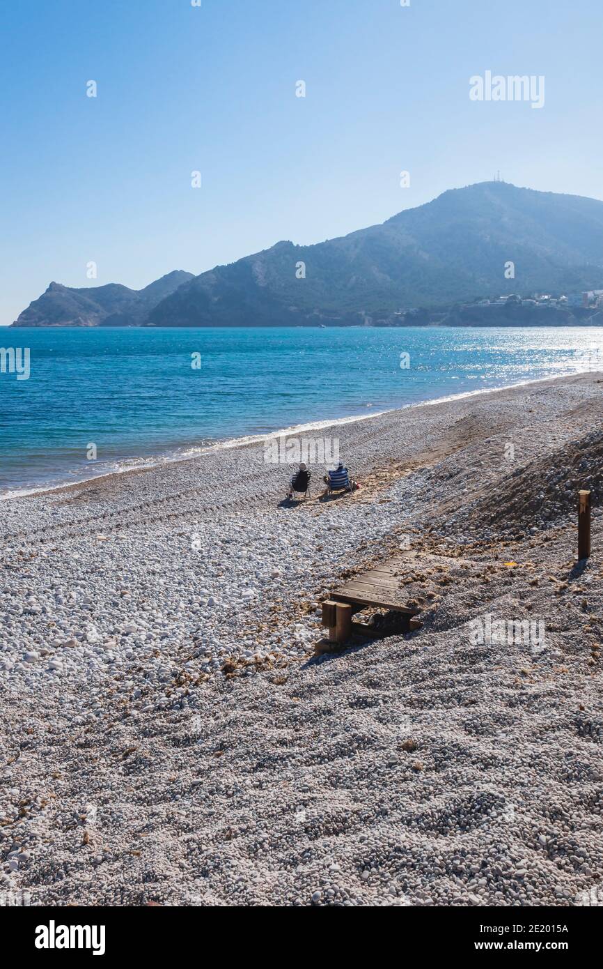 Touristes assis à la plage détruite entre des tas de pierre après la tempête Gloria en janvier 2020, Albir, Costa Blanca, Espagne Banque D'Images