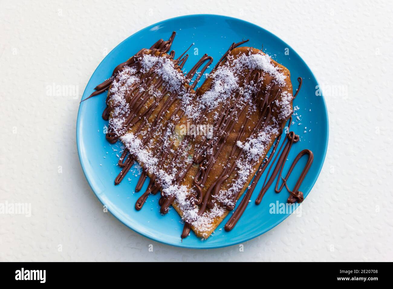 Crêpe en forme de coeur avec crème au chocolat et noix de coco râpée sur  plaque bleue et fond blanc. Délicieux dessert sucré Photo Stock - Alamy