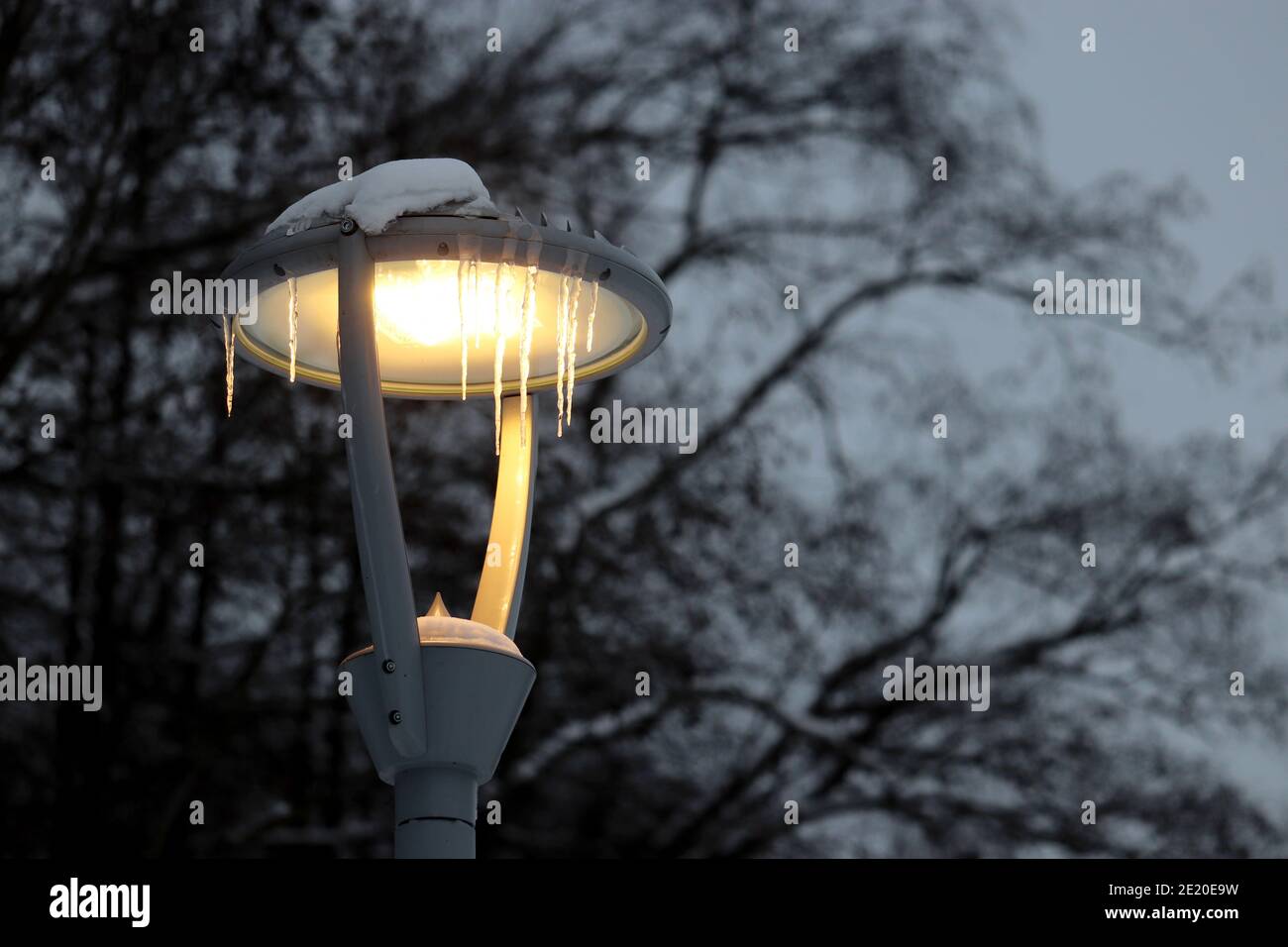 Lampe à LED brillante recouverte de glaçons sur fond d'arbres d'hiver. Éclairage électrique le soir, lanterne de rue à économie d'énergie Banque D'Images