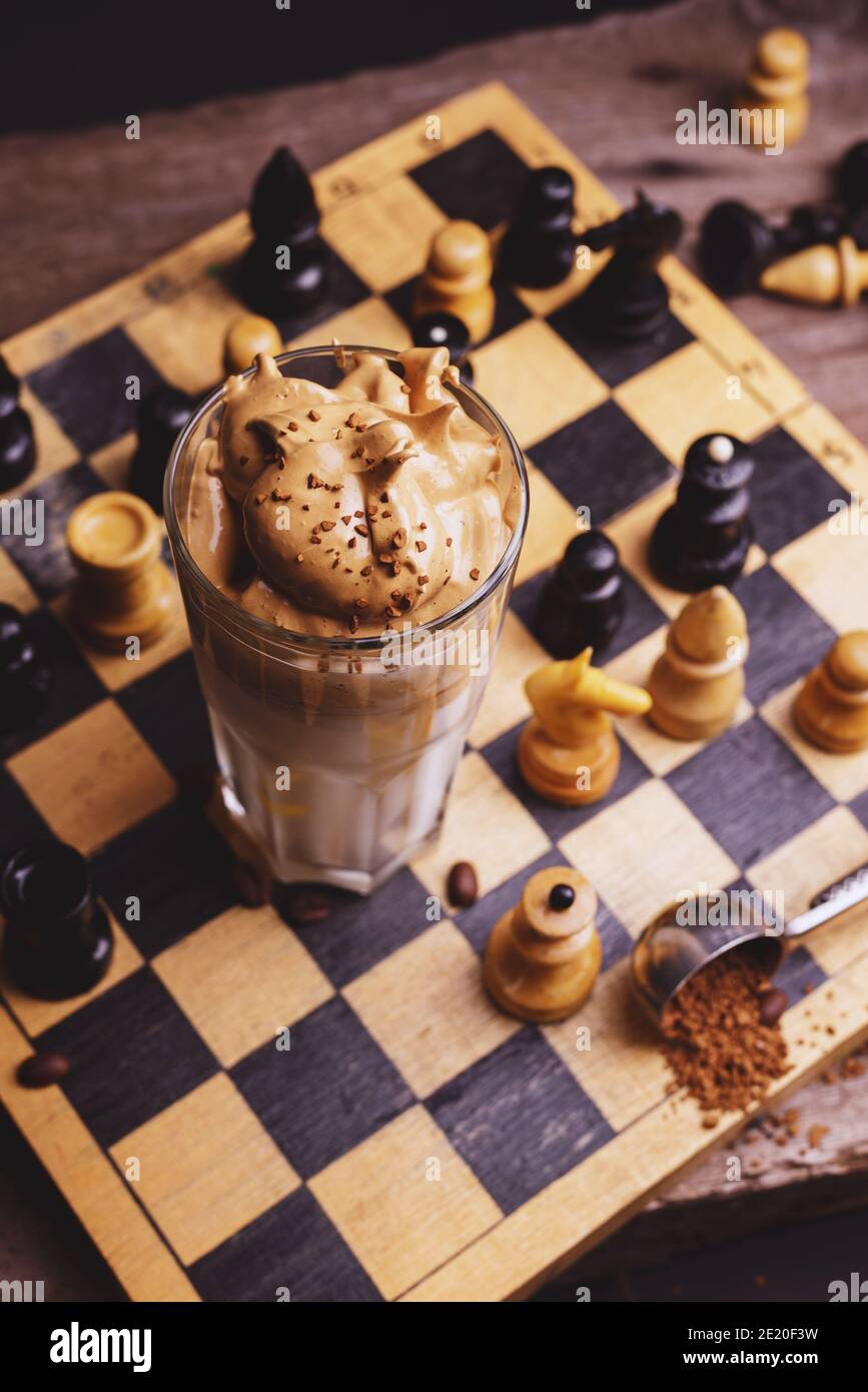 Café Dalgona. Boisson fouettée à glacer avec café instantané populaire en Corée cocktail crémeux dans de grands verres décorés d'échecs sur chessboard en bois Banque D'Images