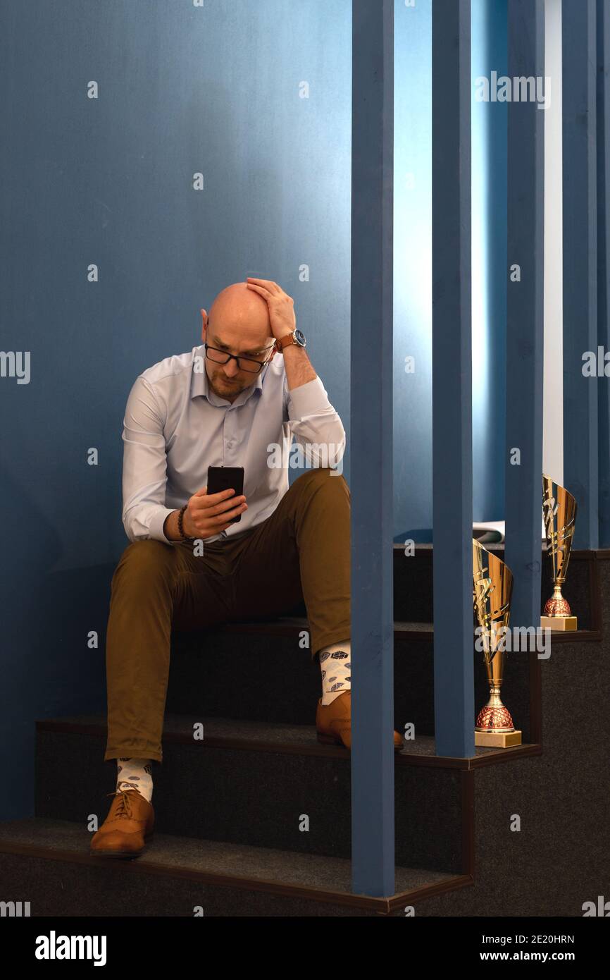homme d'âge moyen sérieux avec un regard perplexe lisant un message ou un article d'actualité sur son téléphone portable, tenant votre tête Banque D'Images