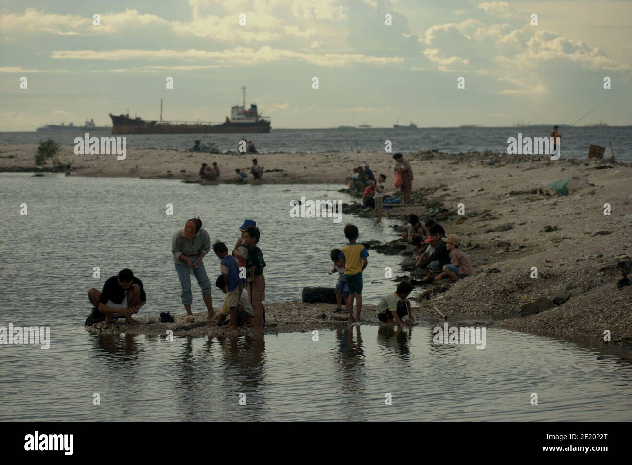 Les personnes ayant des activités récréatives sur la plage de Cilincining, sur la zone côtière de Jakarta, en Indonésie, où la circulation du port de Jakarta peut être vue au loin. Banque D'Images